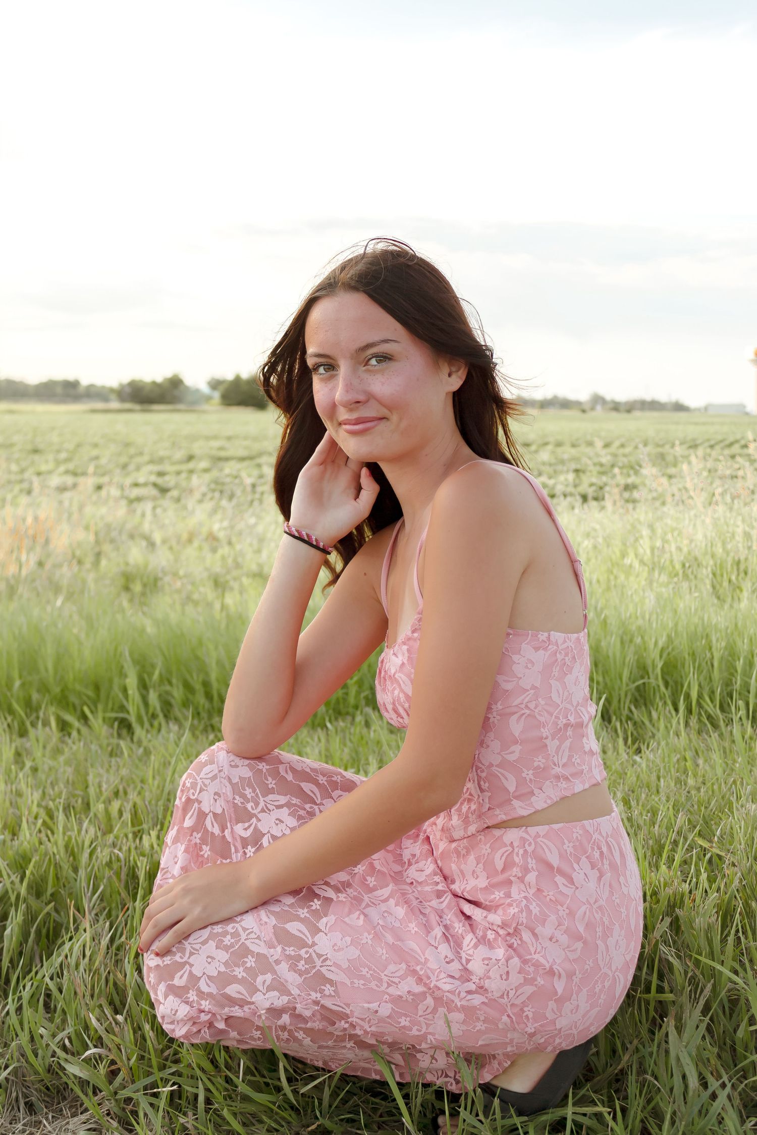 A person in a pink lace dress poses gracefully while sitting in a grassy meadow.