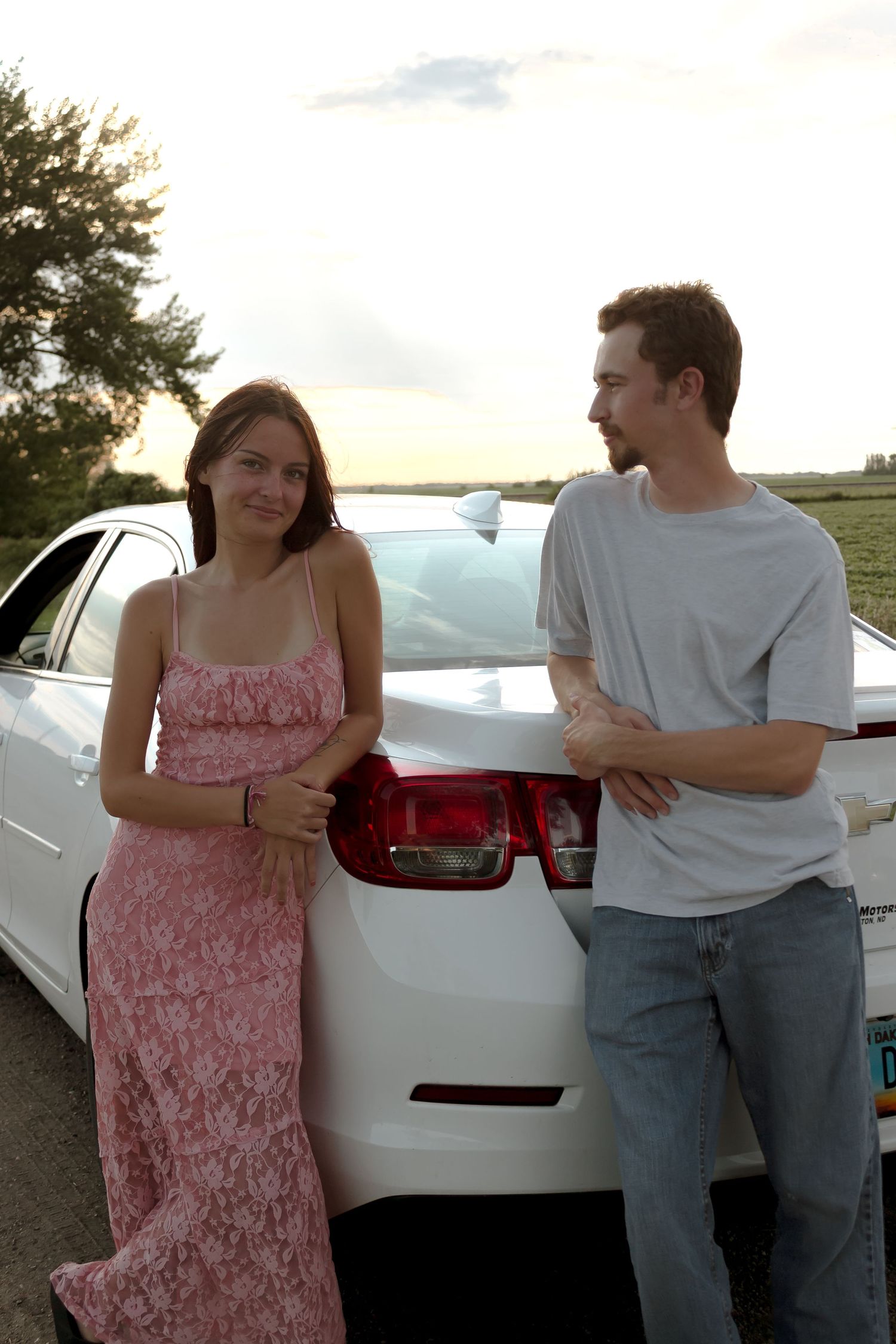 A couple stands beside a white car during golden hour.