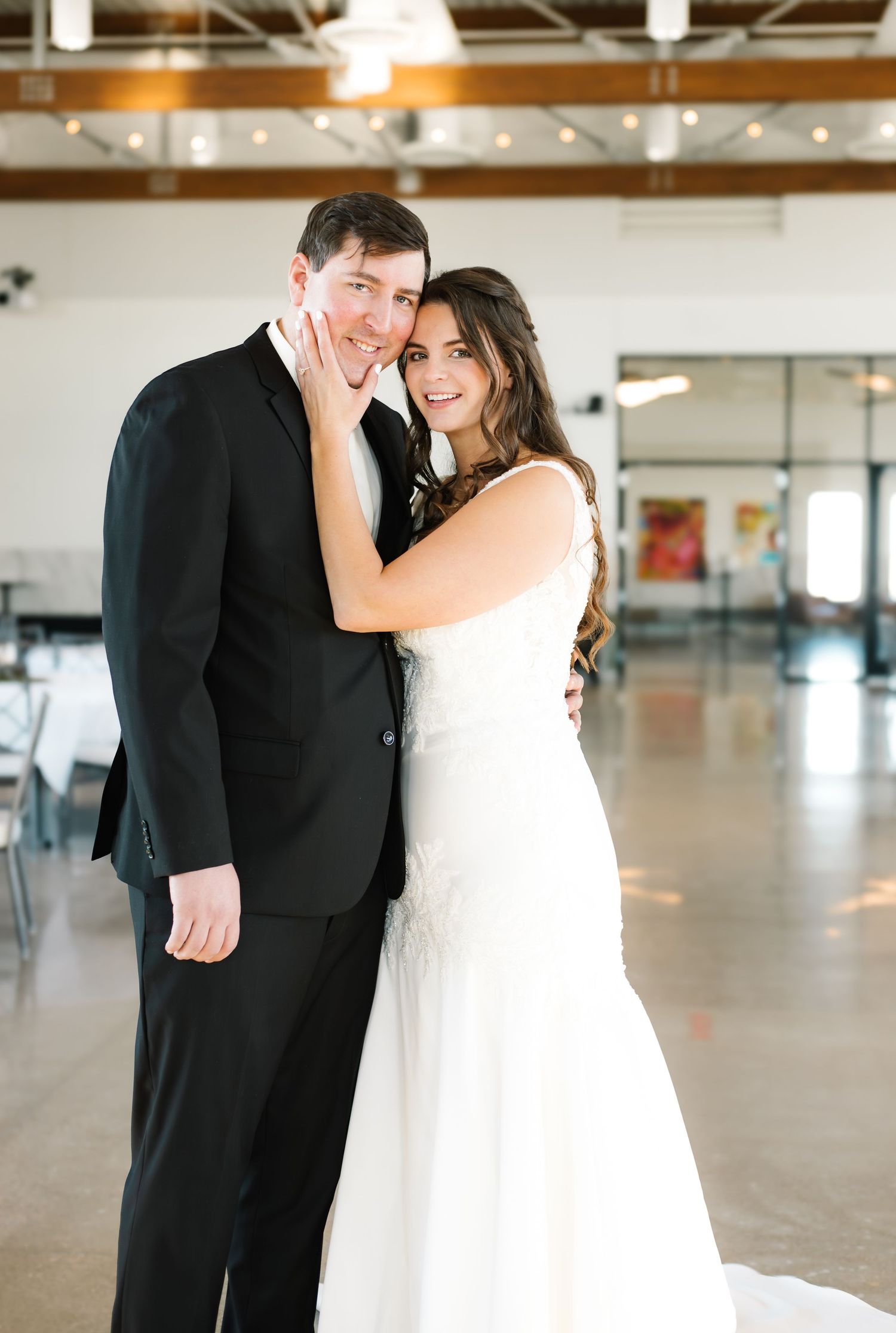 Bride in white gown and groom in black suit pose together smiling in elegant wedding venue.