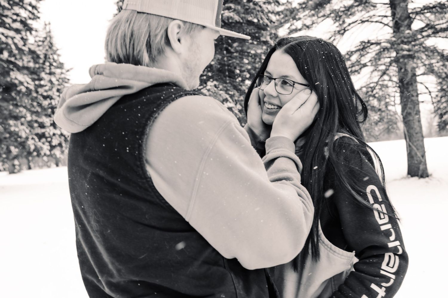 Black and white photo of a couple embracing in snowy winter landscape, man tenderly holding womans face.
