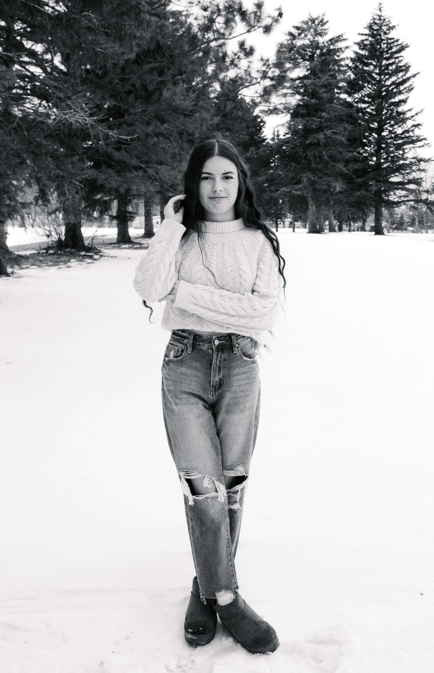 Winter fashion photography featuring distressed jeans and cream sweater against snowy pine forest.