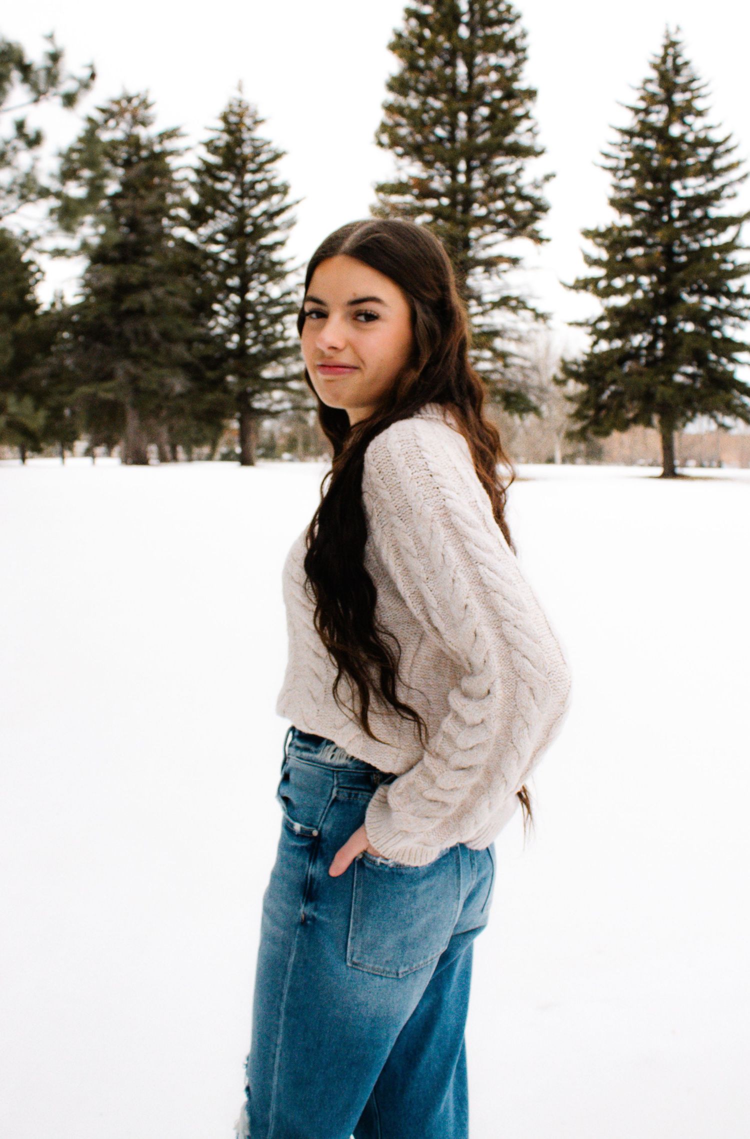 Winter portrait session in the snow with evergreen trees in background.