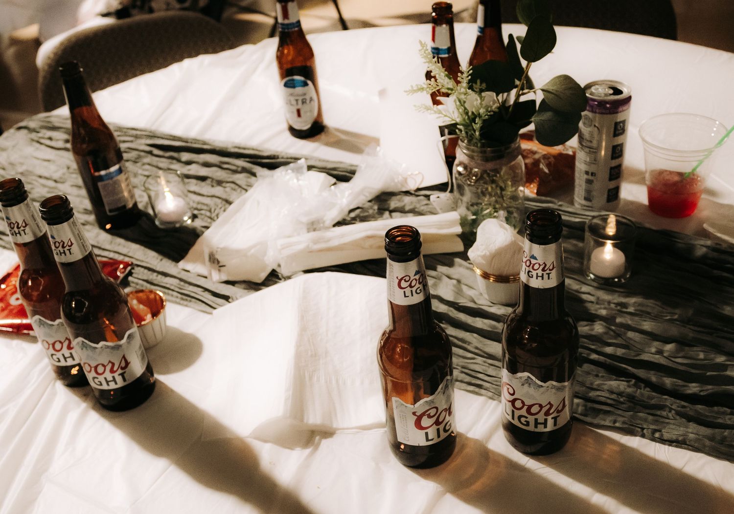 Artistically lit beer bottles displayed on white linens creating dramatic shadows.
