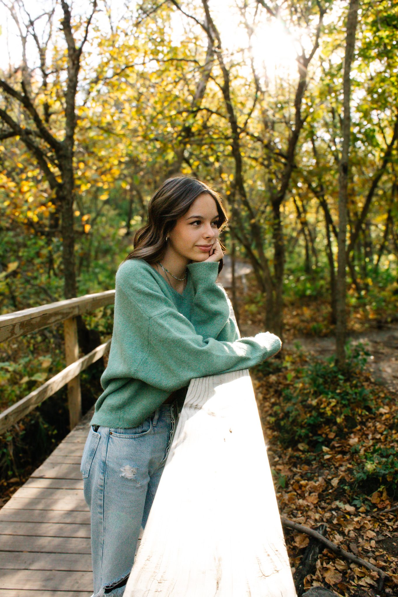 Autumn fashion portrait on wooden bridge wearing mint green sweater and light wash jeans.