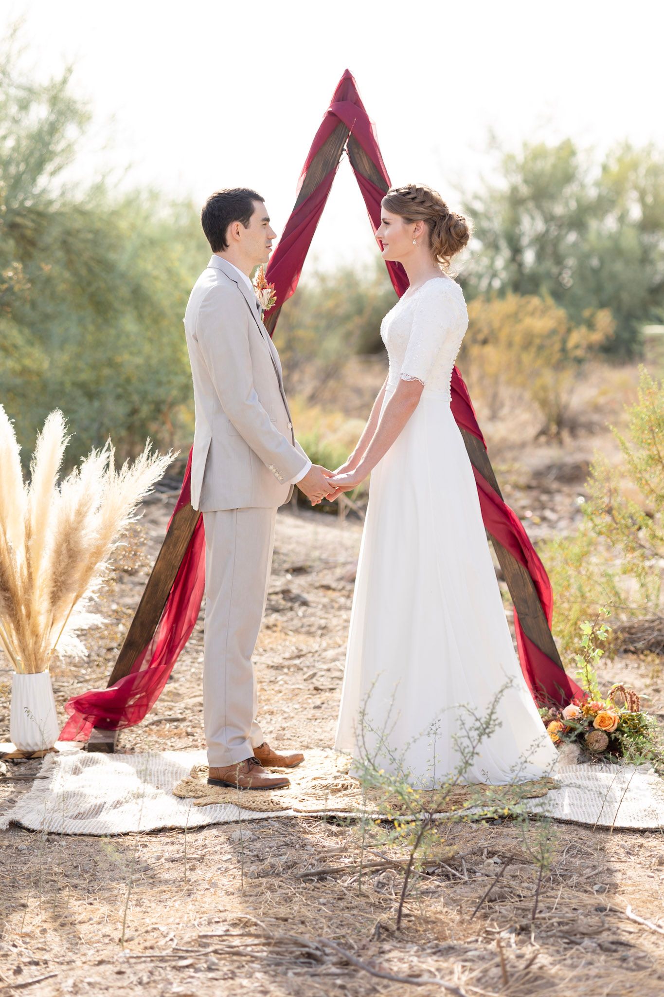 Desert wedding setup with burgundy triangle arch and pampas grass decorations.