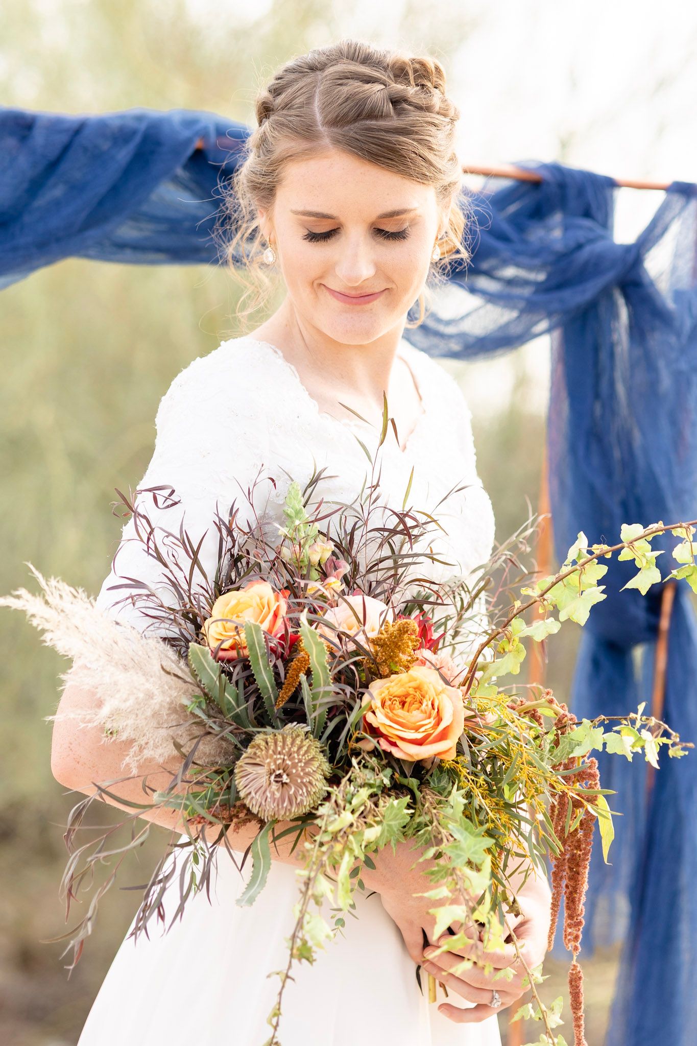 Bride holding natural autumn-colored wedding bouquet with roses and dried elements.