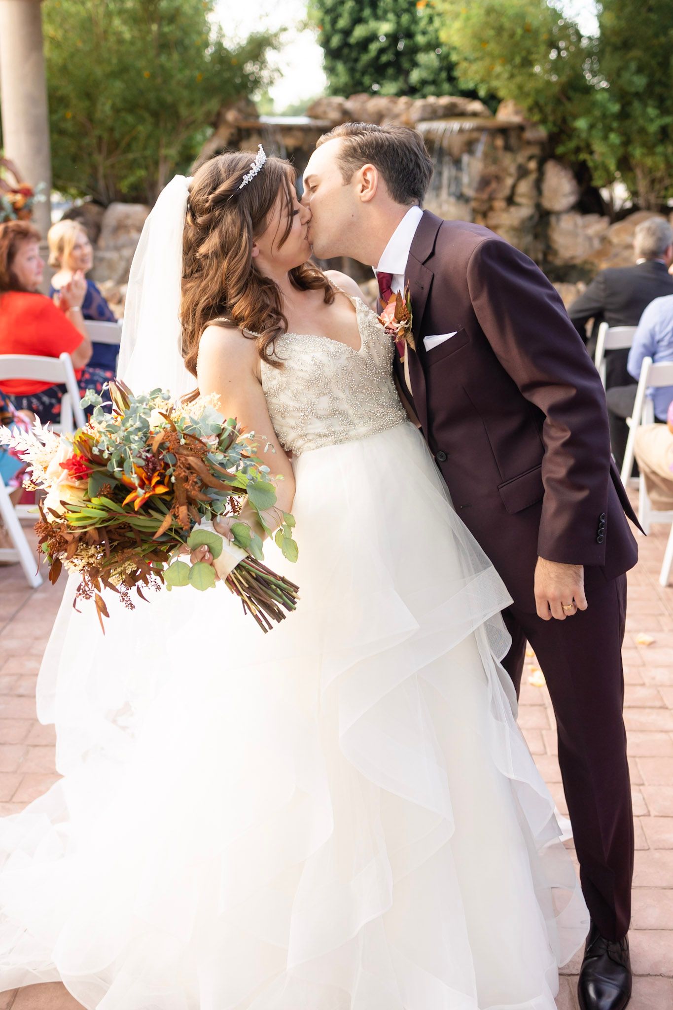 Bride in flowing white gown with train poses at outdoor wedding venue with stone details.