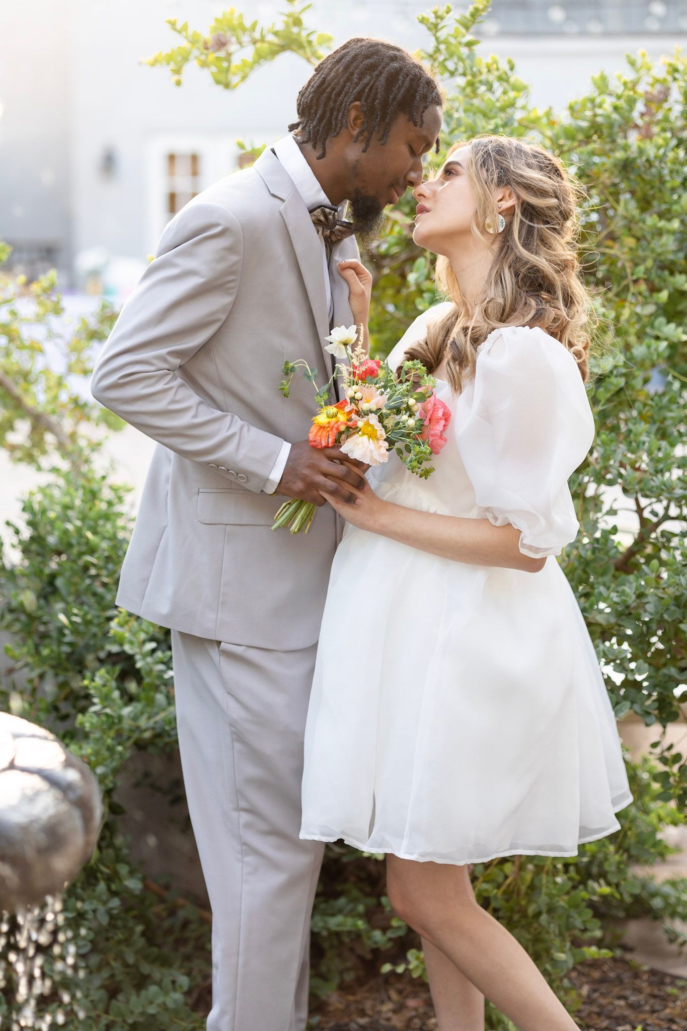 Newlyweds share tender moments on outdoor steps with white dress and light gray suit.