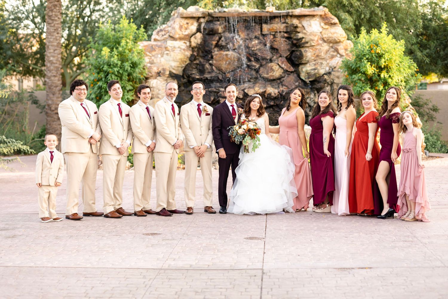 Wedding party members line up outdoors wearing coordinated formal attire.