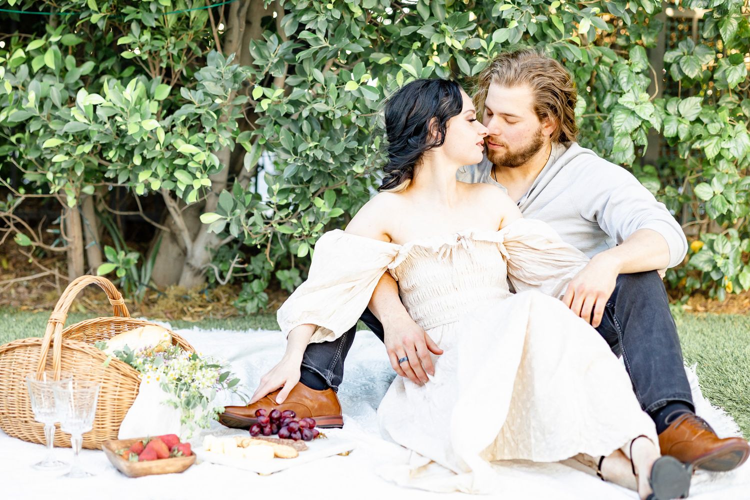 A couple enjoys a romantic outdoor picnic with fresh fruit and wicker baskets in a lush garden setting.