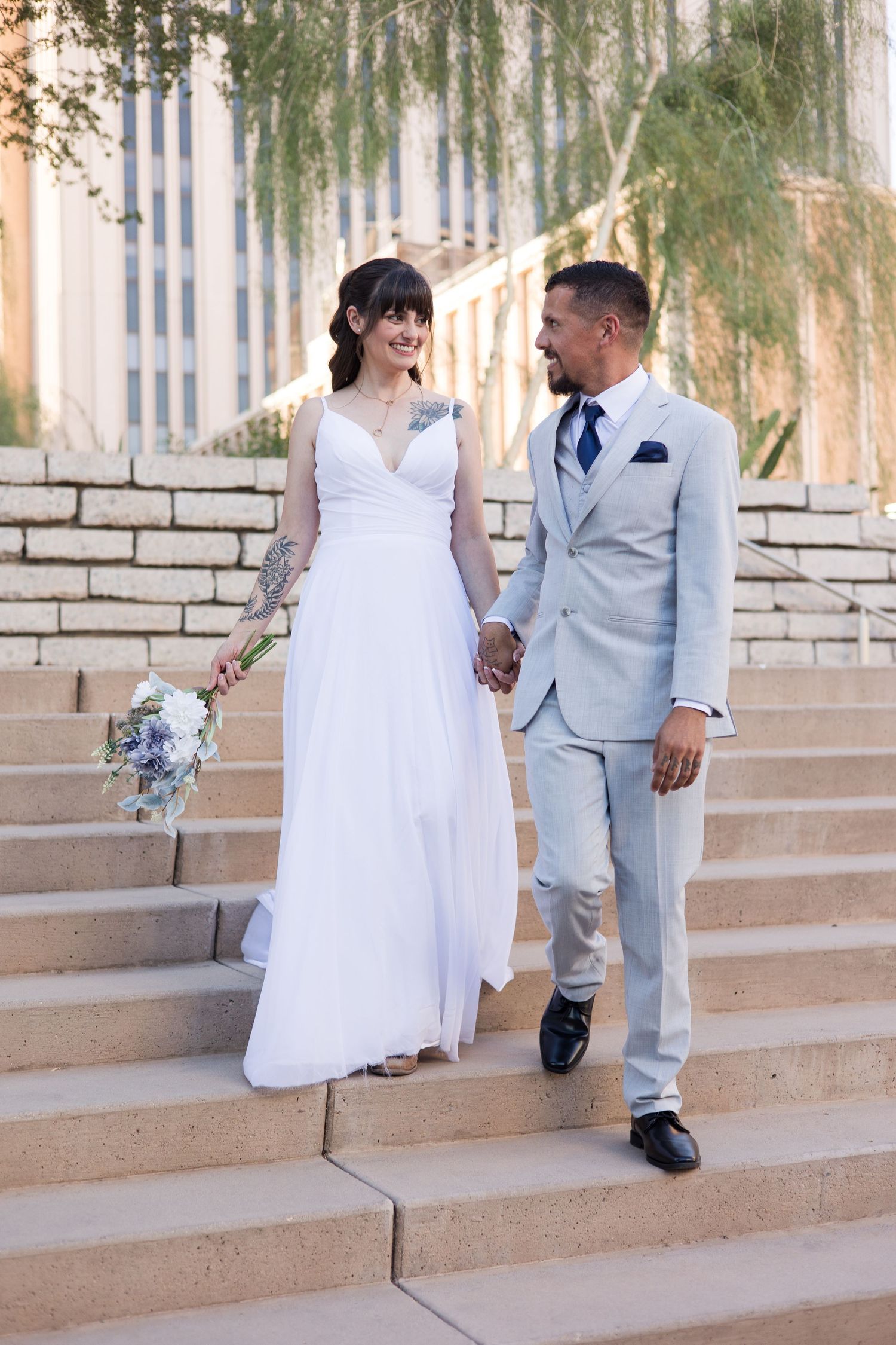 Newlyweds walk hand in hand down stone steps at an outdoor venue in Phoenix, AZ.