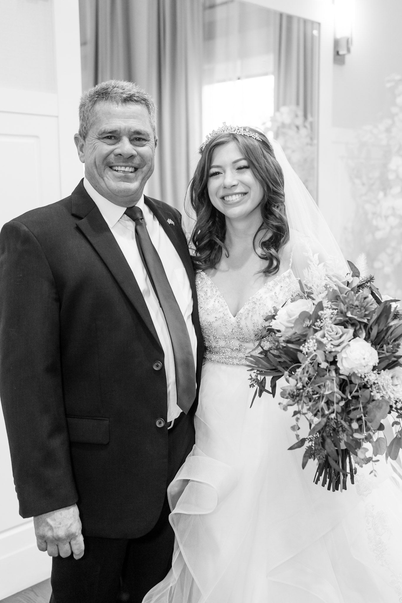 A bride in a white dress smiles while holding a colorful bouquet next to someone in a dark suit.