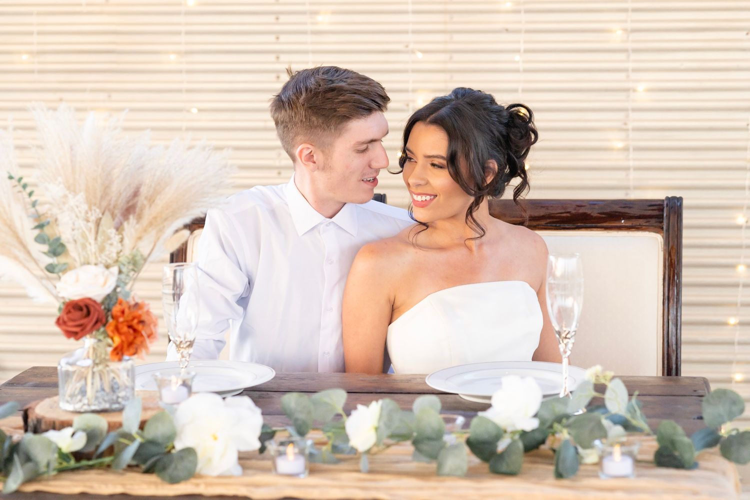 Romantic outdoor table setting with white linens, floral arrangements, and delicate glassware at sunset.