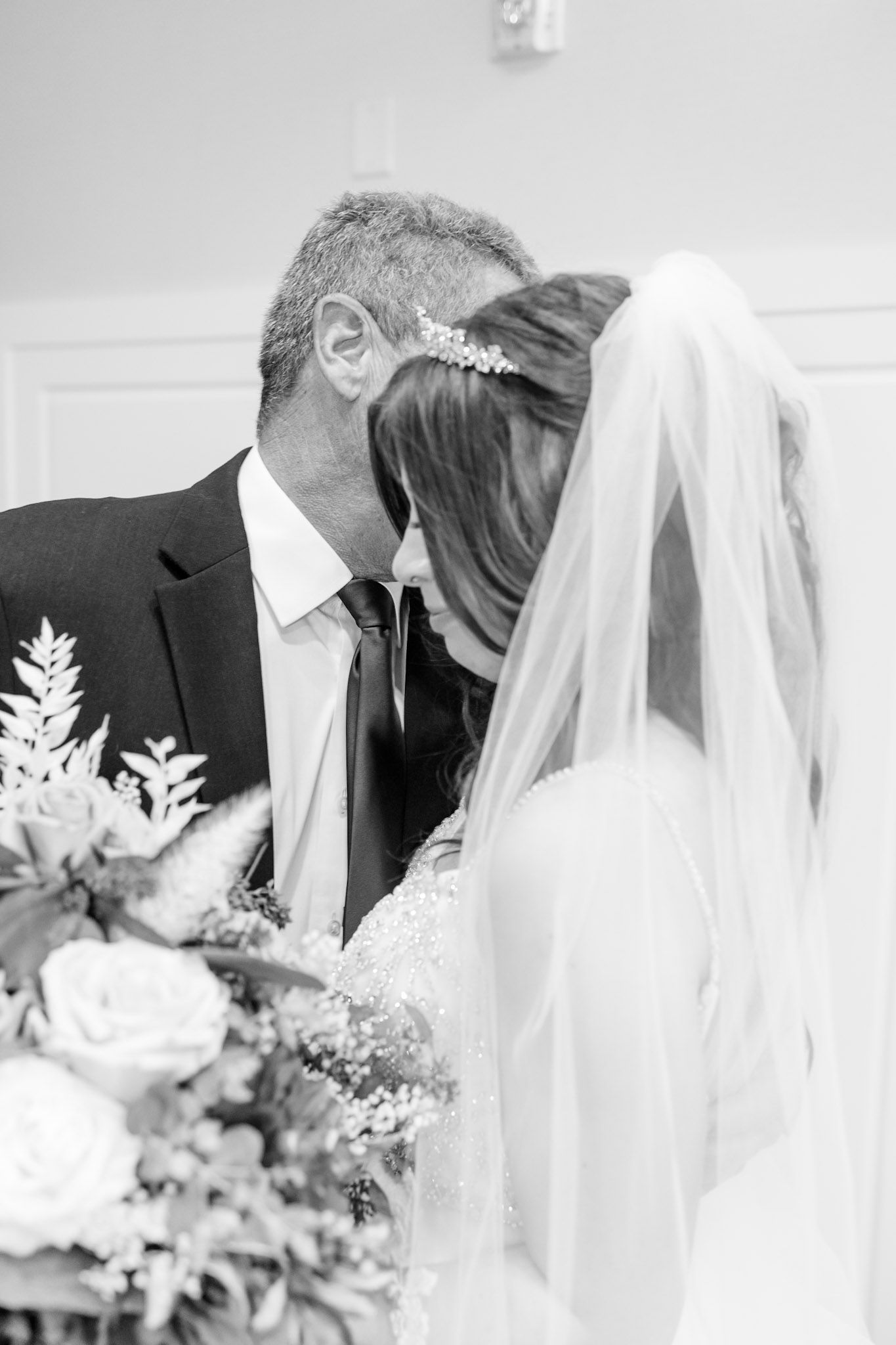 Tender black and white wedding ceremony moment with floral bouquet in foreground.