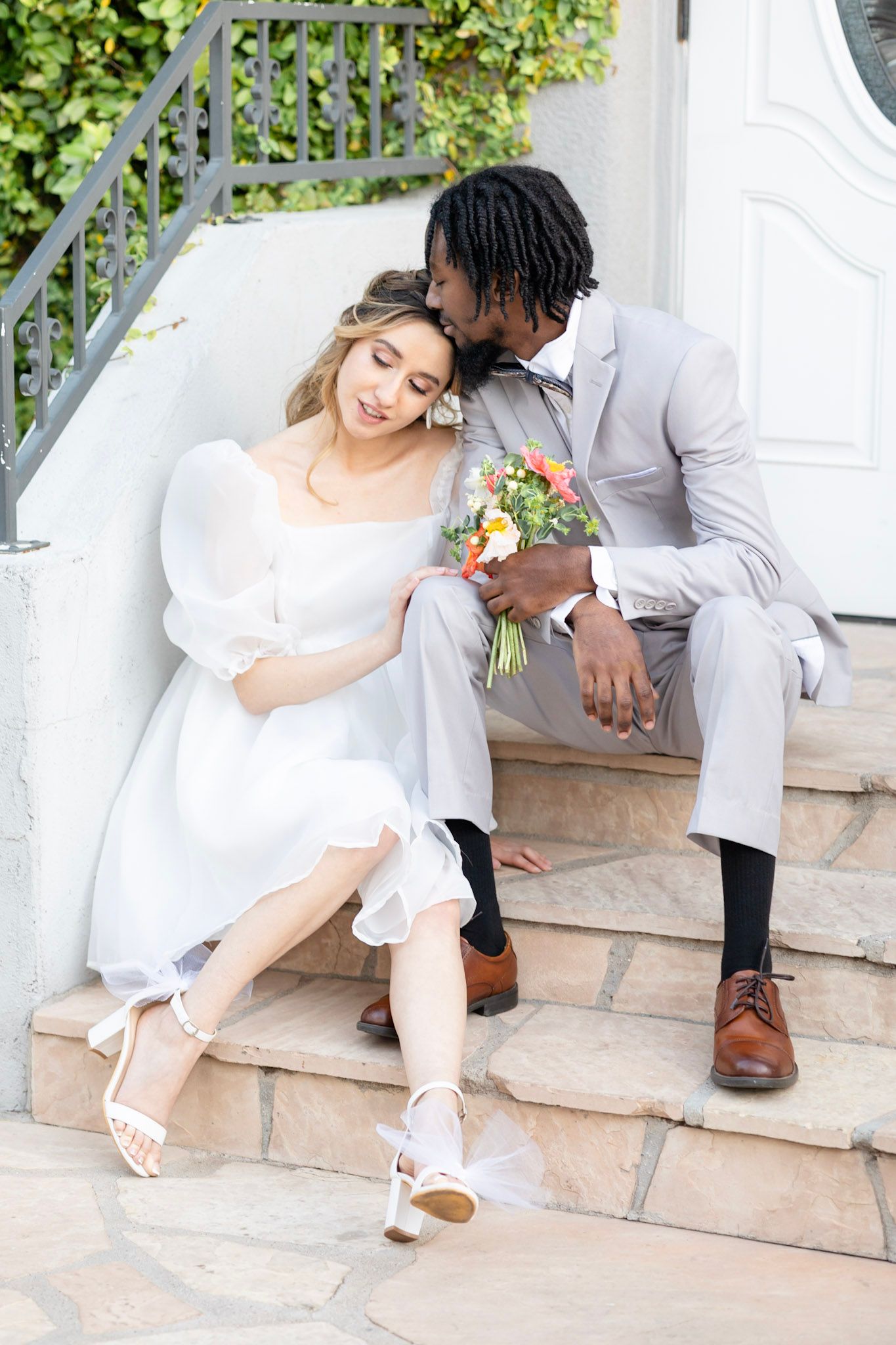 Wedding couple relaxes on tiled steps with bride in white dress and groom in gray suit.