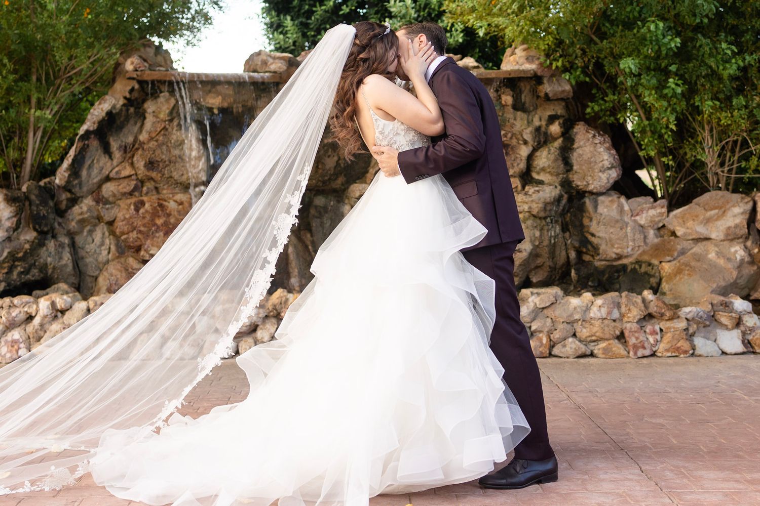 Wedding couple photographed against a rustic stone wall backdrop with flowing veil.