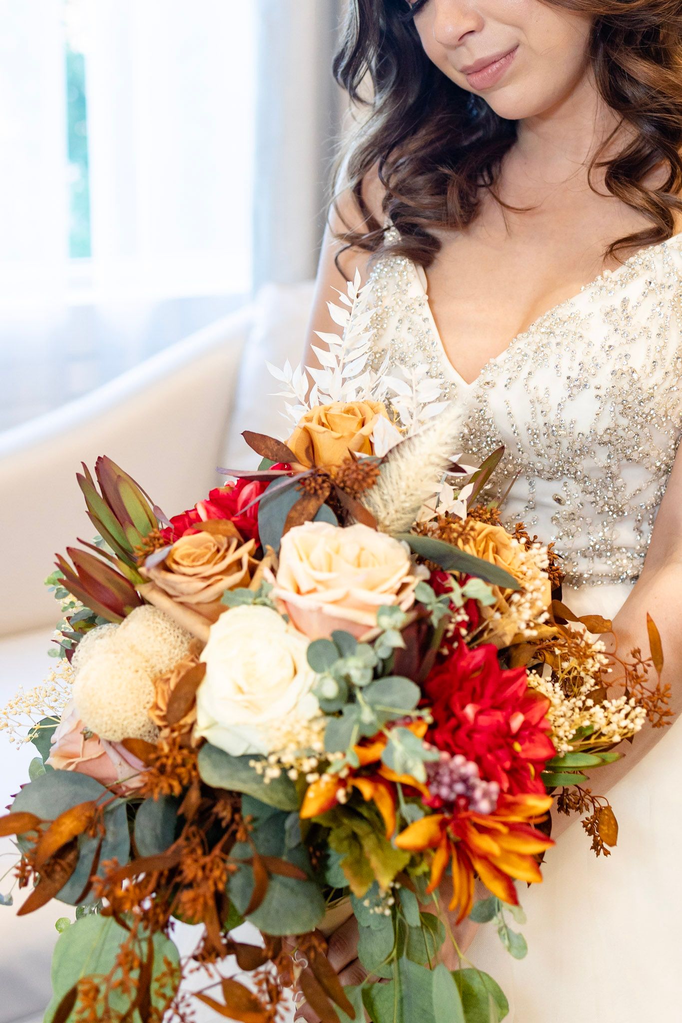 Fall-themed bridal bouquet with peach roses, eucalyptus, and burgundy accents.