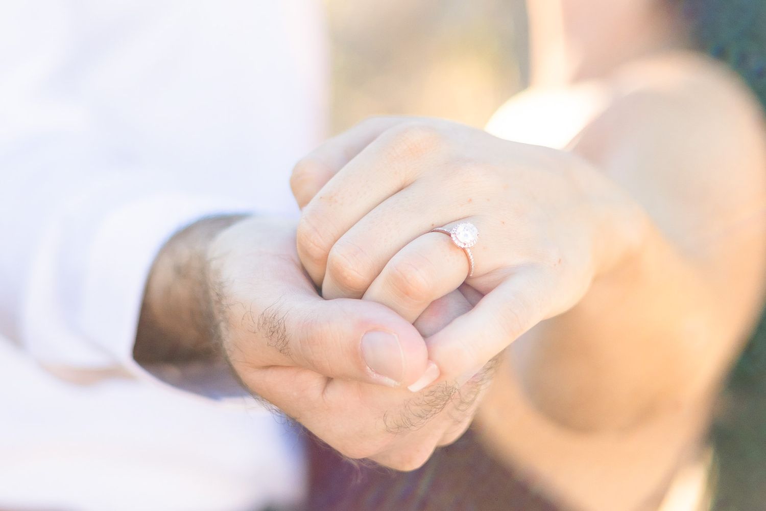 Close up view of hands holding each other showing an engagement ring with soft dreamy lighting effect.
