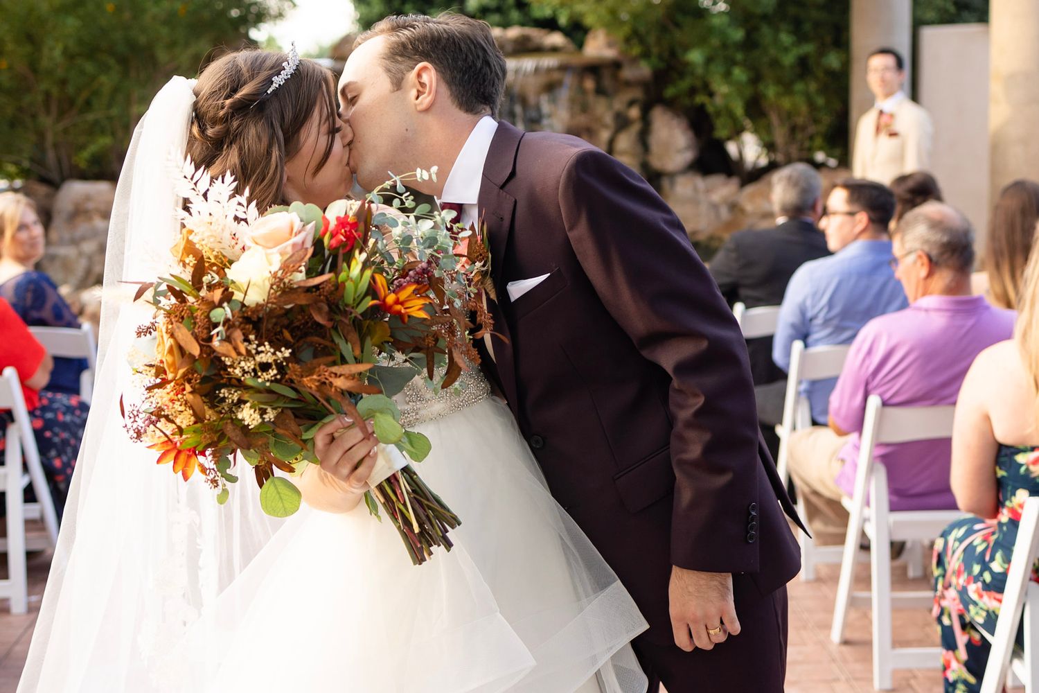 Outdoor wedding ceremony with guests seated in white chairs against a natural backdrop.