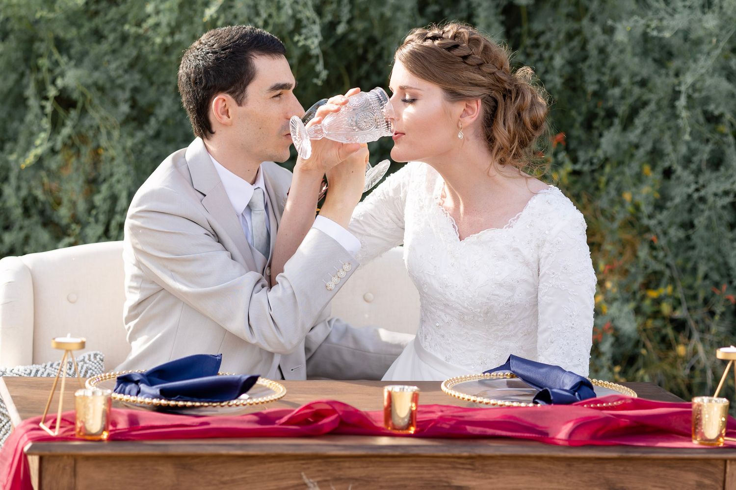 Wedding couple shares intimate moment at rustic outdoor table with blue and red decor.