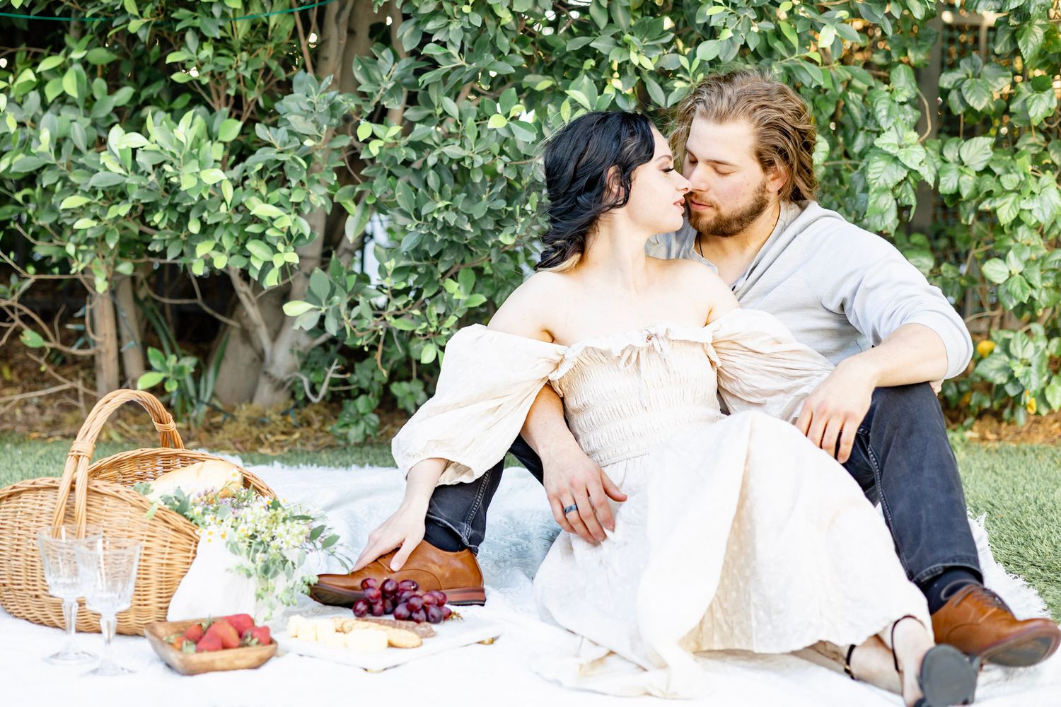 Romantic picnic scene with couple lounging on blanket surrounded by fruit and greenery.