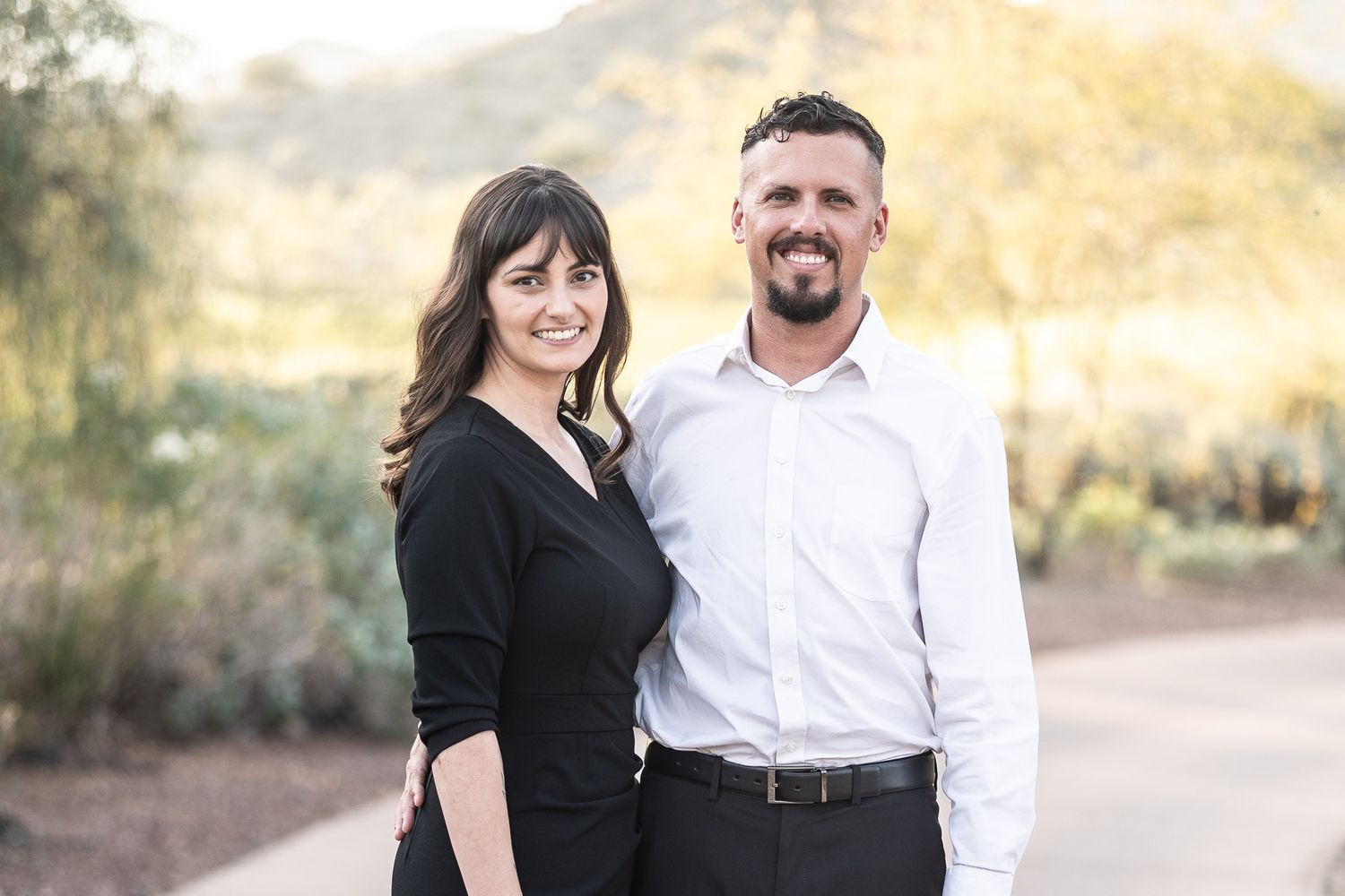 A couple poses together outdoors during golden hour in a desert landscape setting.