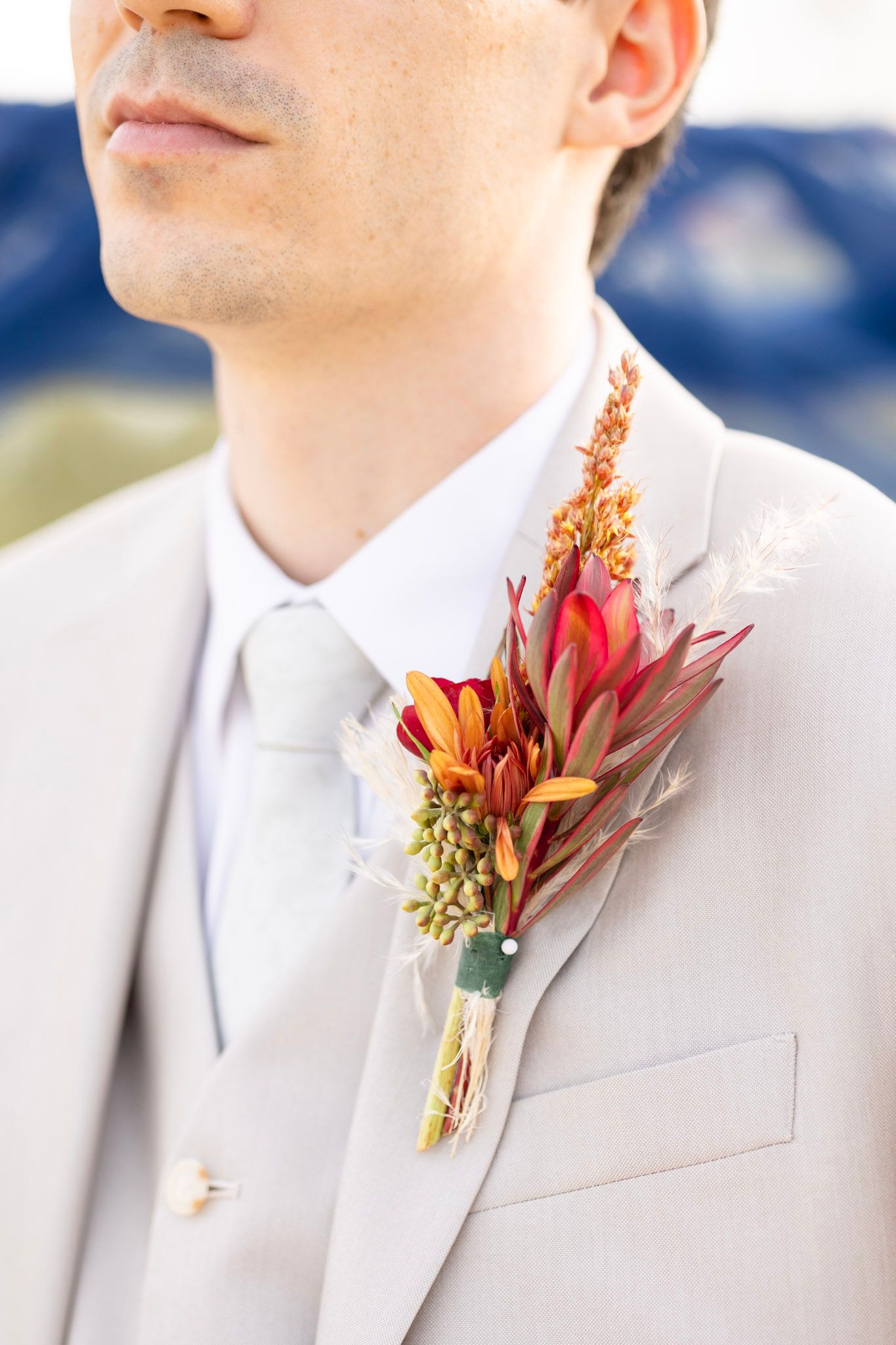 Close-up of red and orange fall boutonniere on light grey suit lapel.