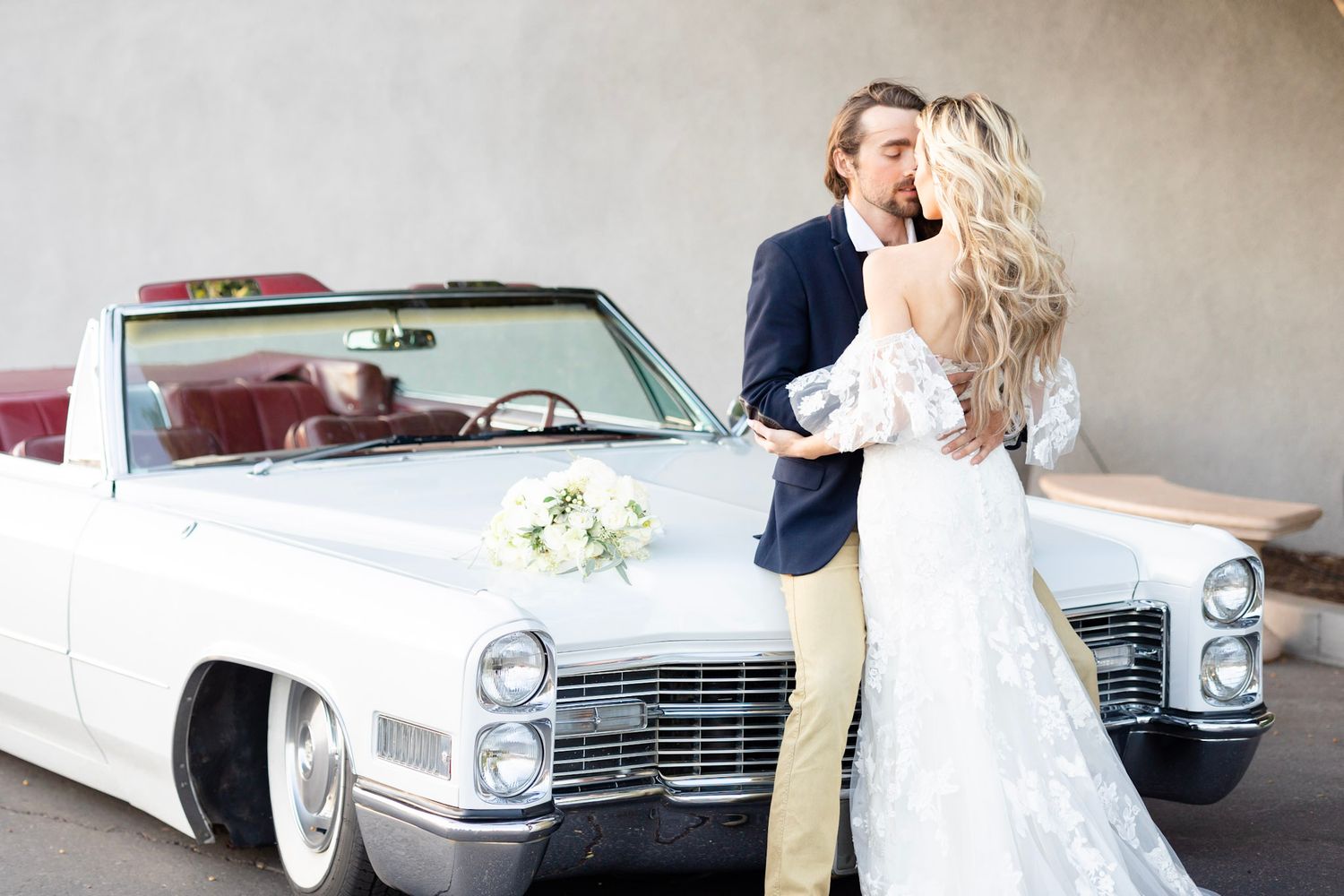 Classic white vintage car decorated with floral arrangements for wedding transportation.
