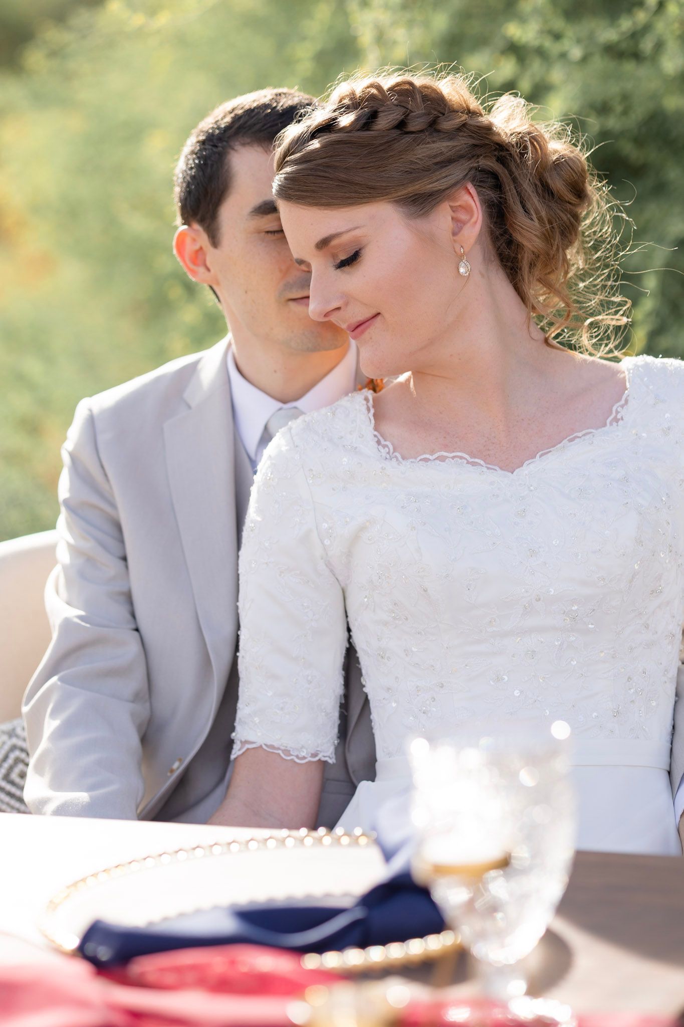 Couple in white and grey attire share intimate moment at outdoor wedding table.