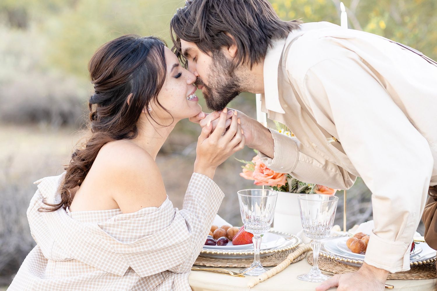 Intimate outdoor dining setup with white candles and floral arrangements at sunset.