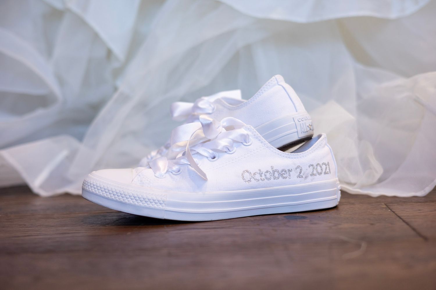 White bridal sneakers with laces and wedding date displayed against soft fabric backdrop.