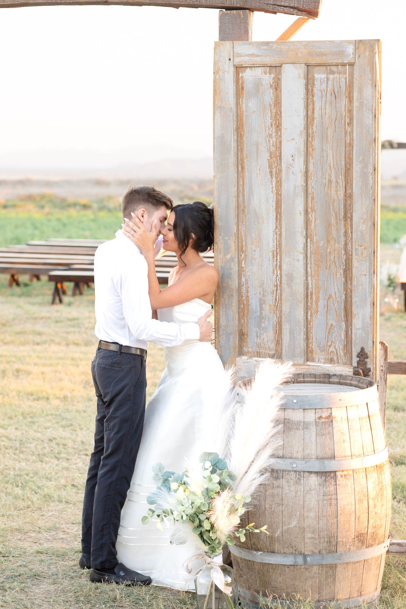 Wedding couple shares intimate moments by weathered barn walls and vintage barrel decor.