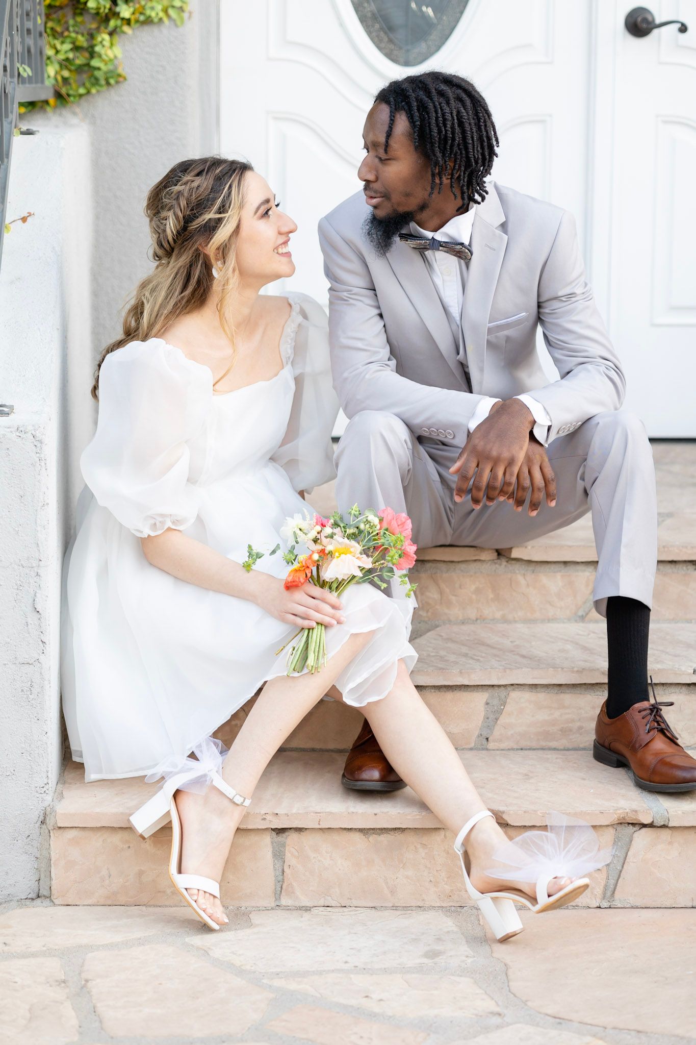 Romantic wedding couple sitting on stone steps surrounded by greenery in an intimate outdoor setting.