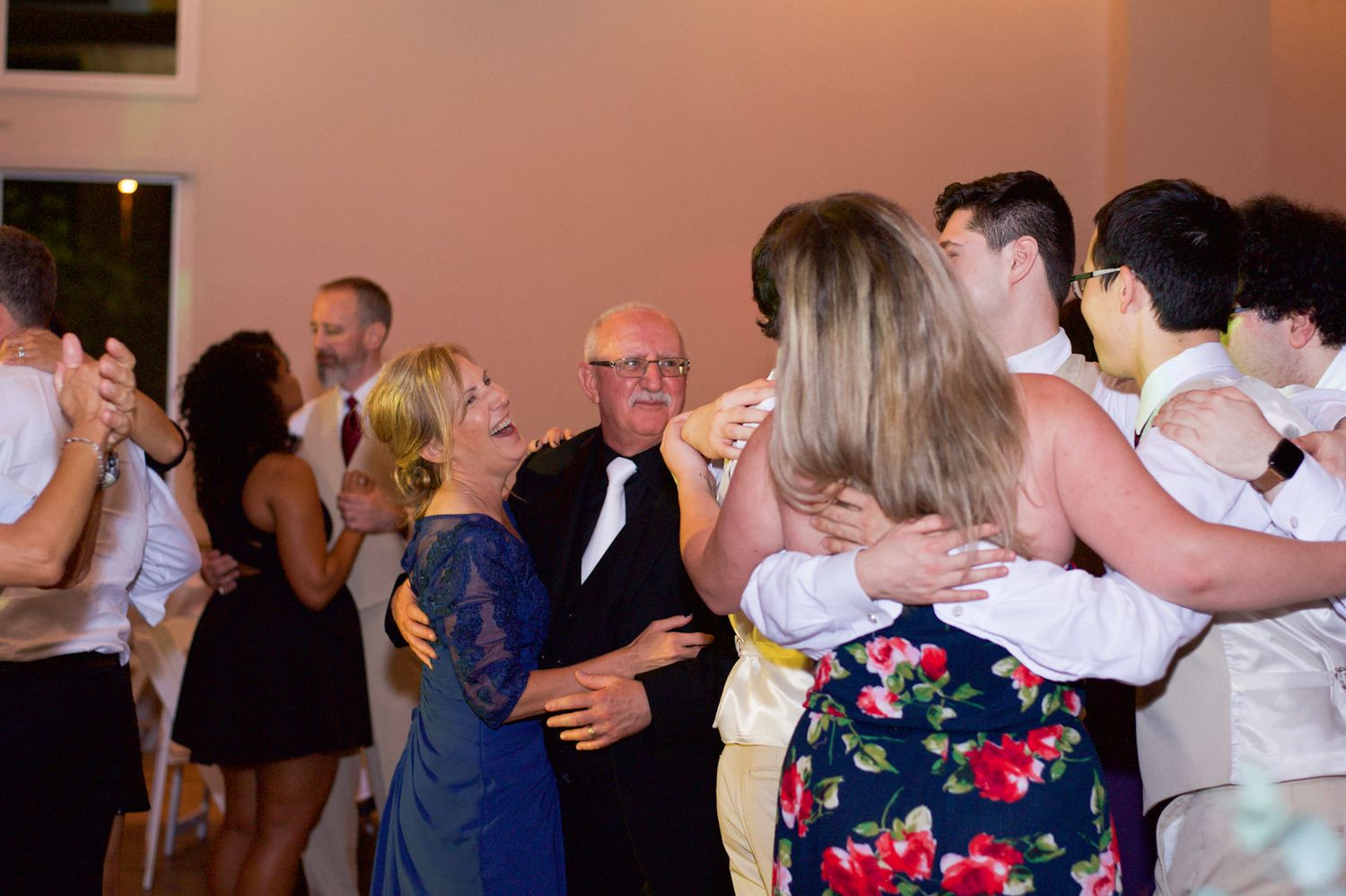 Guests dancing and celebrating at an indoor wedding reception with pink lighting accents.