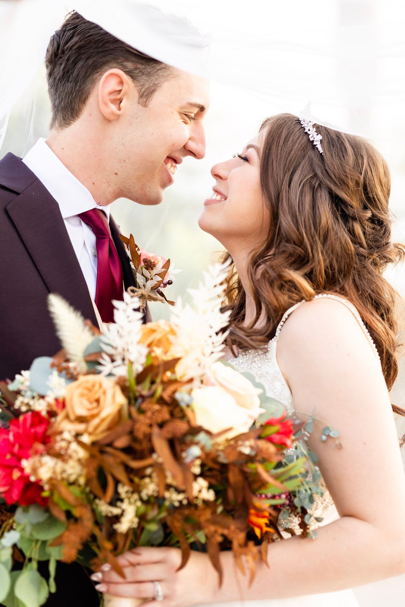 Romantic wedding couple shares intimate moment while holding autumn-colored bouquet.