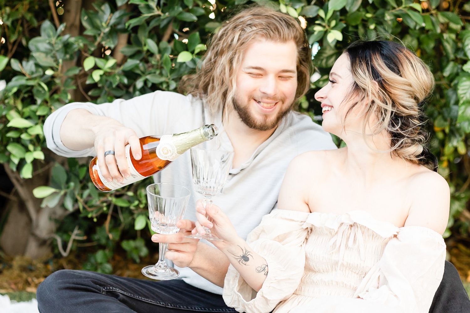 A couple shares a romantic moment while pouring and enjoying champagne together in an outdoor garden setting.