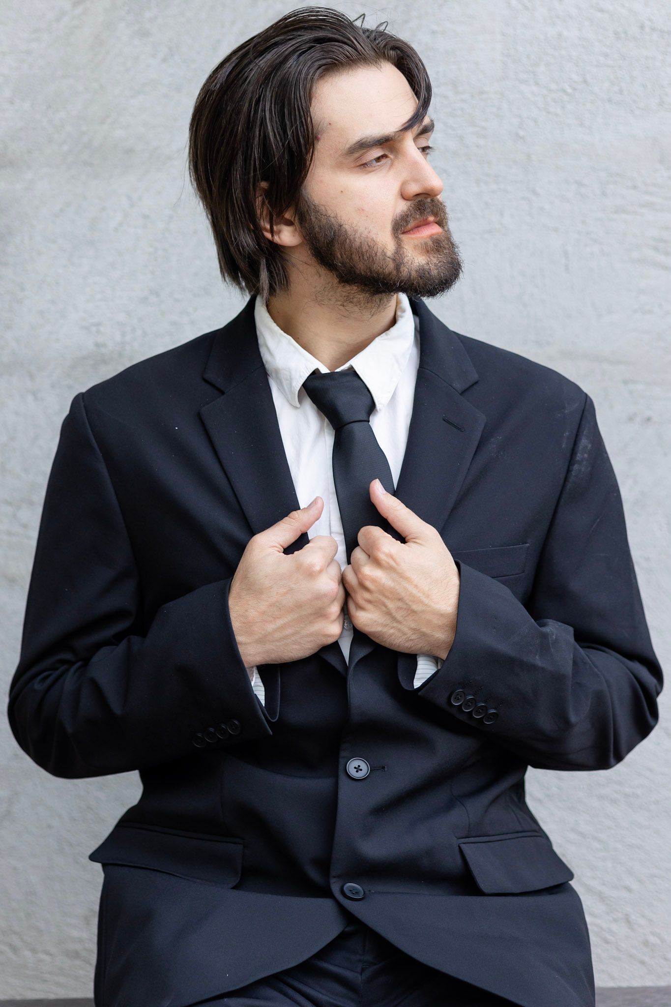 Groom in black suit adjusting his jacket in artistic portrait series.