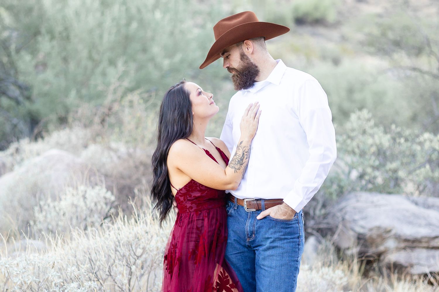 Desert engagement photoshoot with couple in western attire against sage brush landscape.