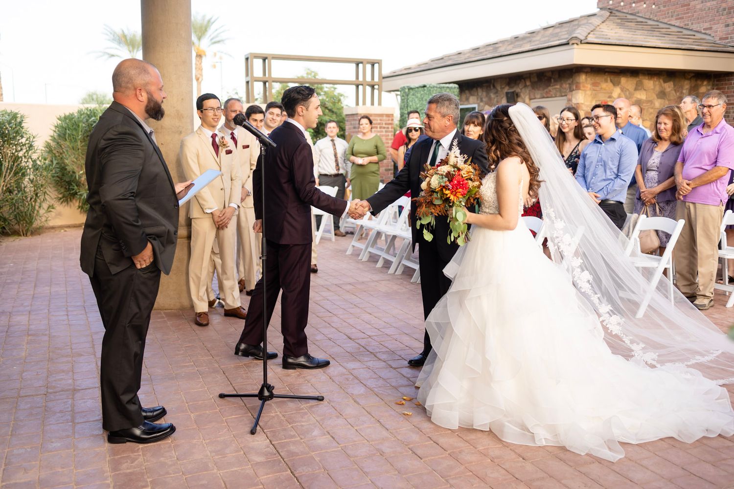 Wedding ceremony guests seated outdoors at a venue with stone and brick architecture.
