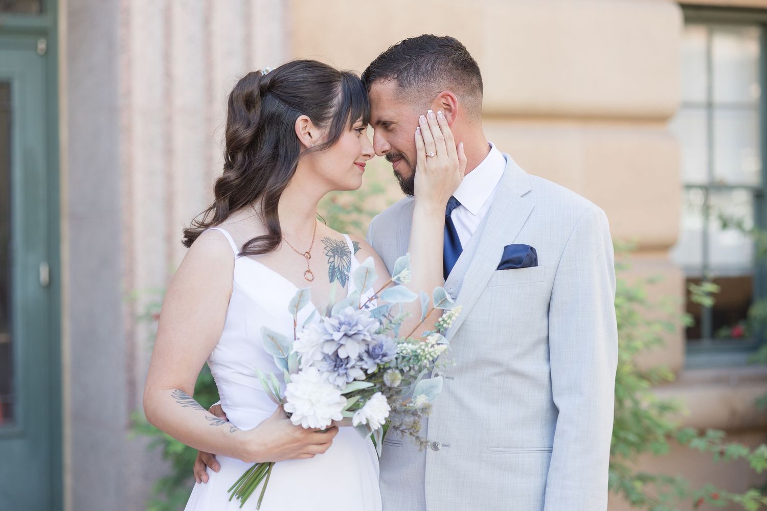 Newlyweds in white and light gray attire pose for romantic portraits outdoors.