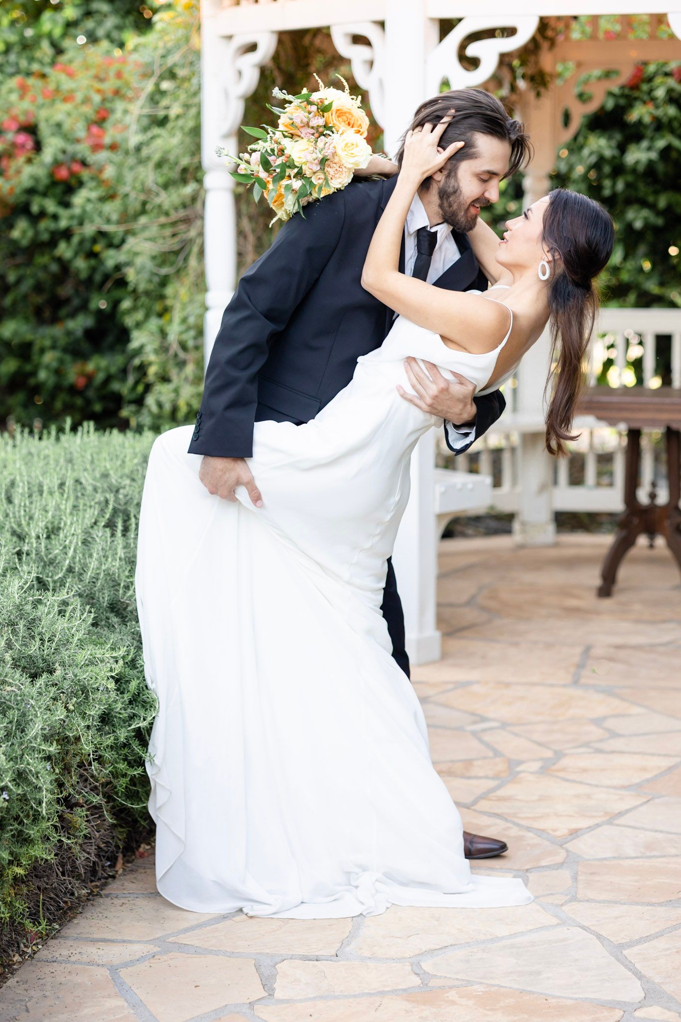 Romantic dip pose on stone patio surrounded by garden greenery.