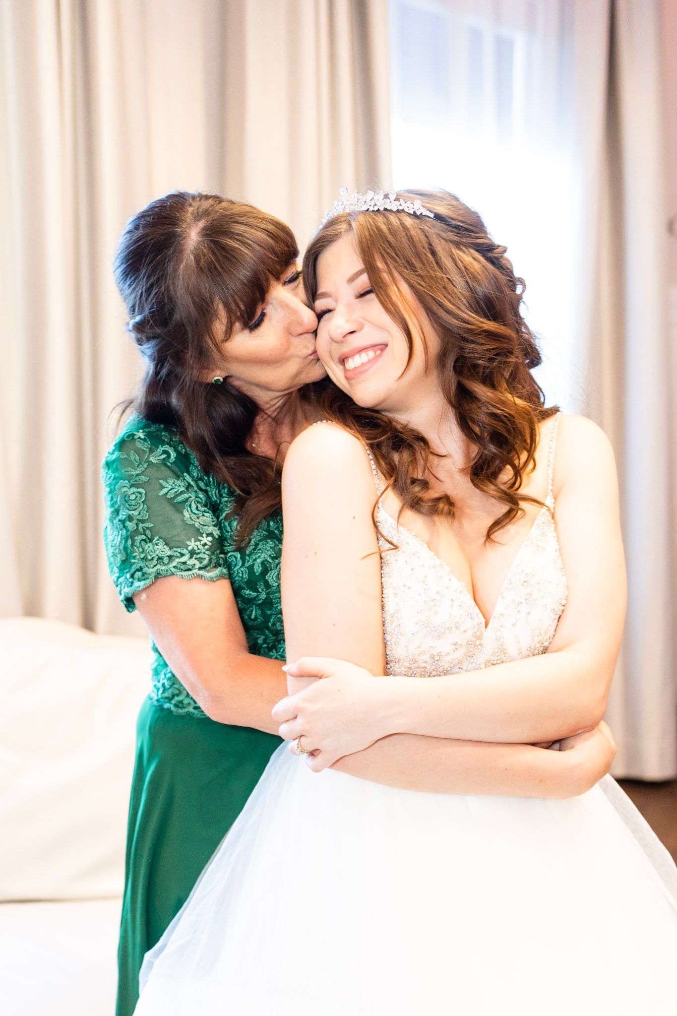 Emotional wedding moment between bride in white and bridesmaid in emerald green dress.