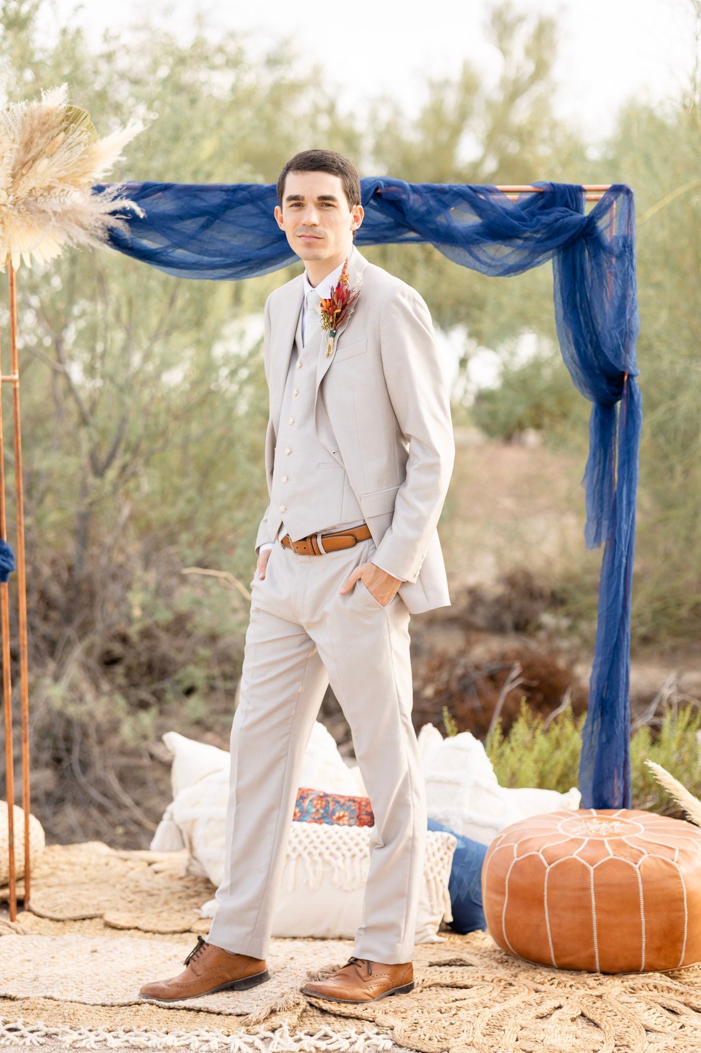 Wedding setup in desert with blue fabric draping and orange poufs on sandy ground.