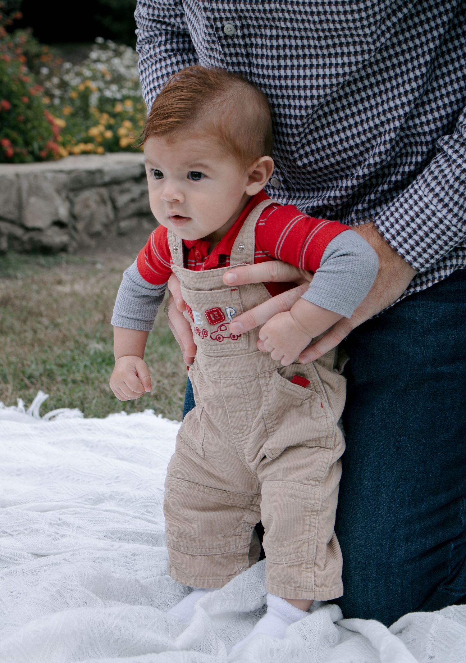 Close-up sequence of a baby in tan overalls and red shirt sitting on a white blanket.