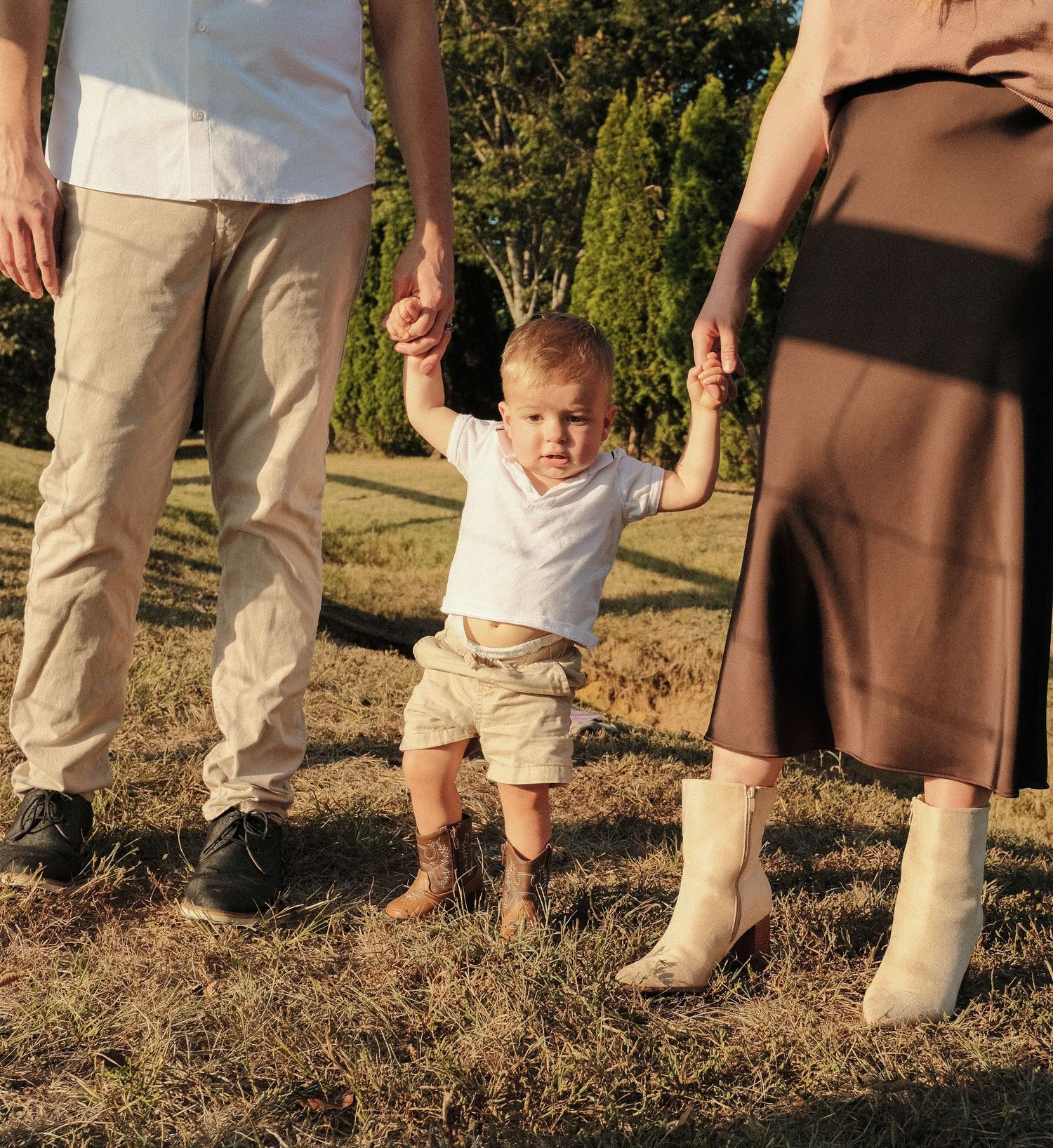 Candid photo showing legs and feet of family members standing together outdoors.