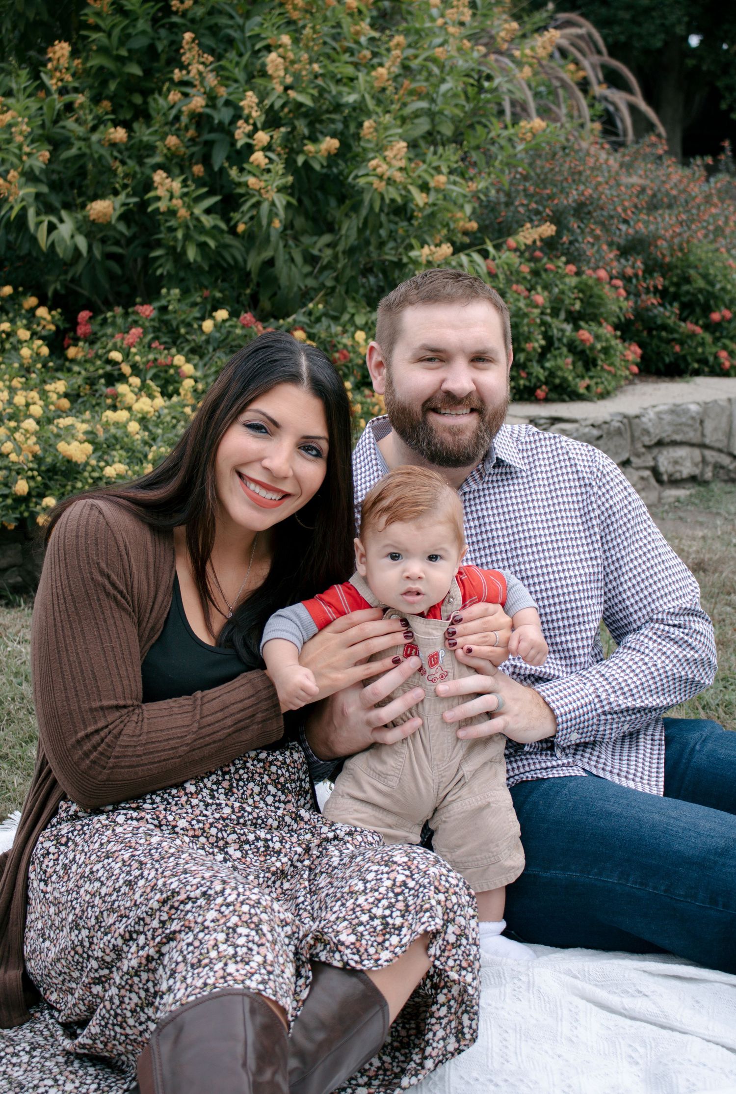 Family sitting together on a white blanket in a garden setting with blooming yellow flowers.