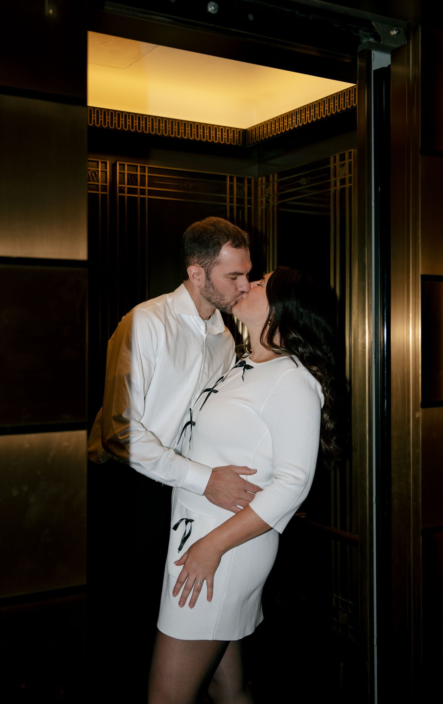 A couple in white shirts share a romantic kiss sequence in an elevator.
