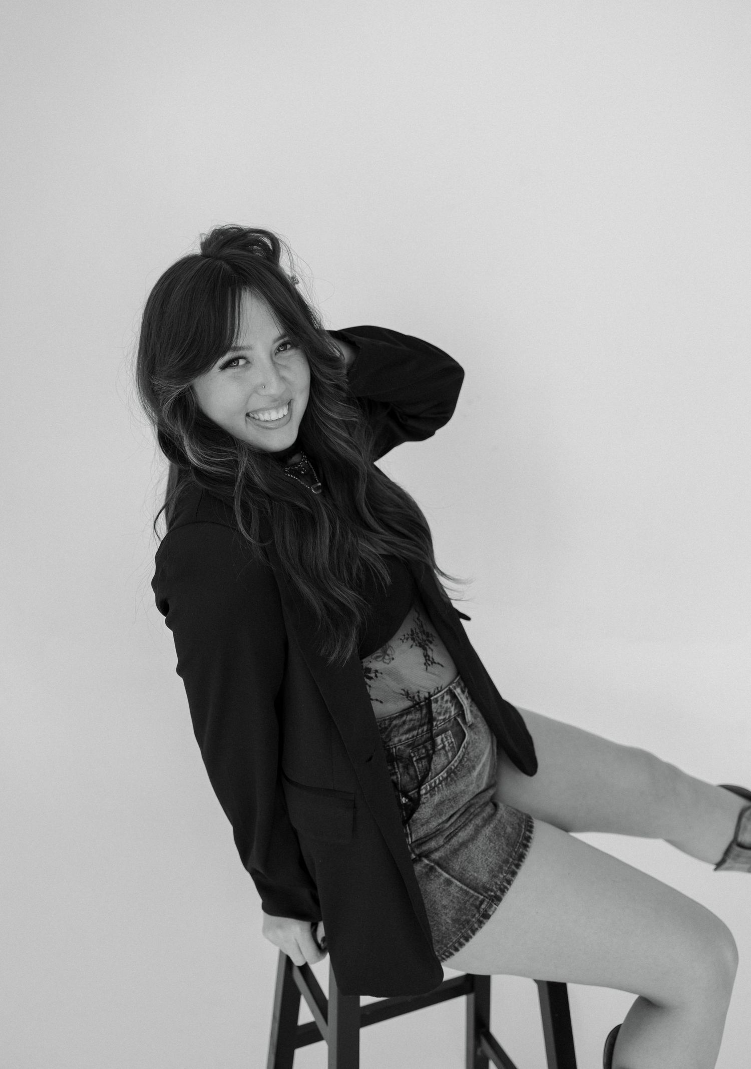 Black and white fashion photo series showing a woman in a blazer and denim posing on a chair against a white backdrop.