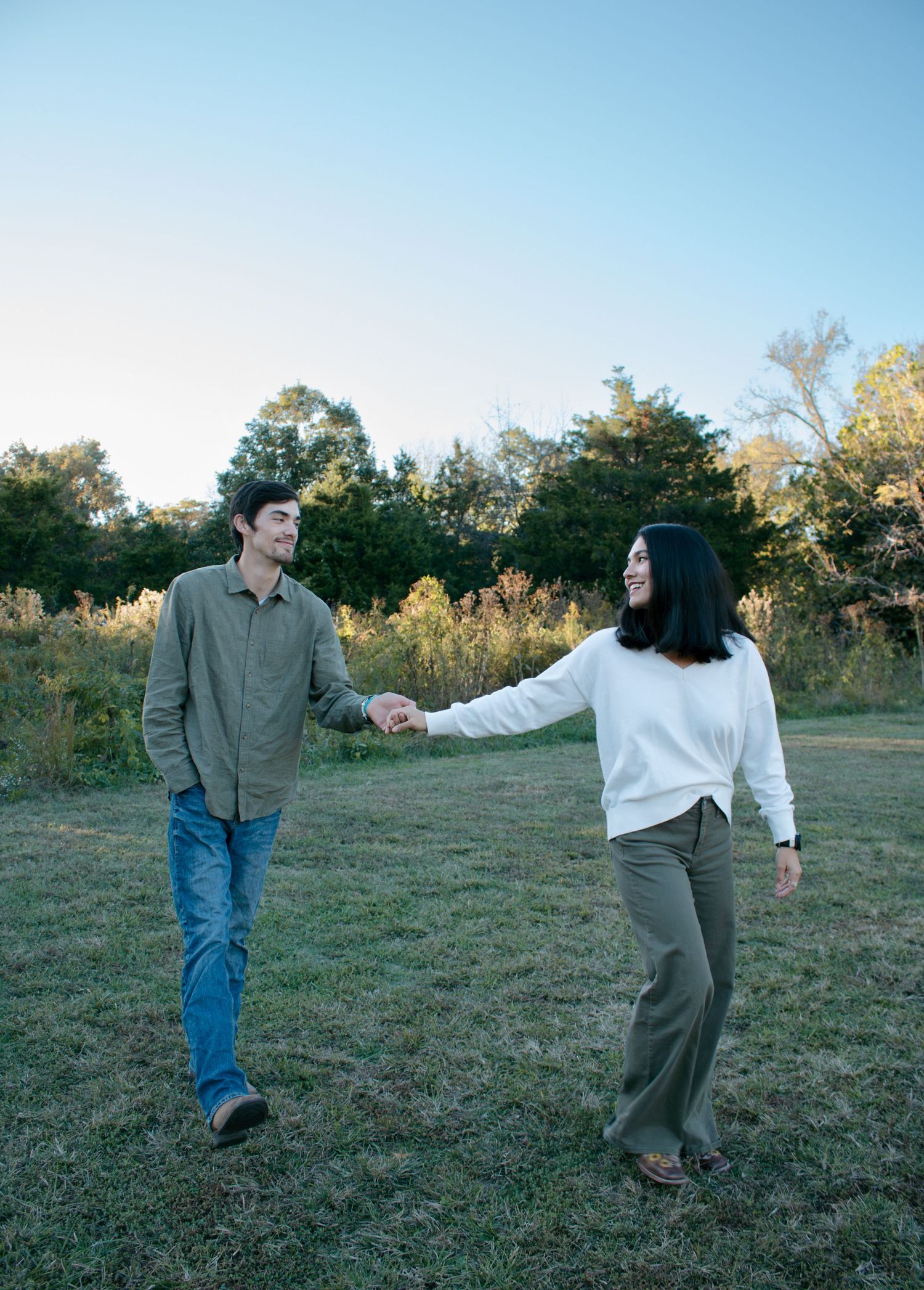 Couple dancing playfully in grassy field at sunset.