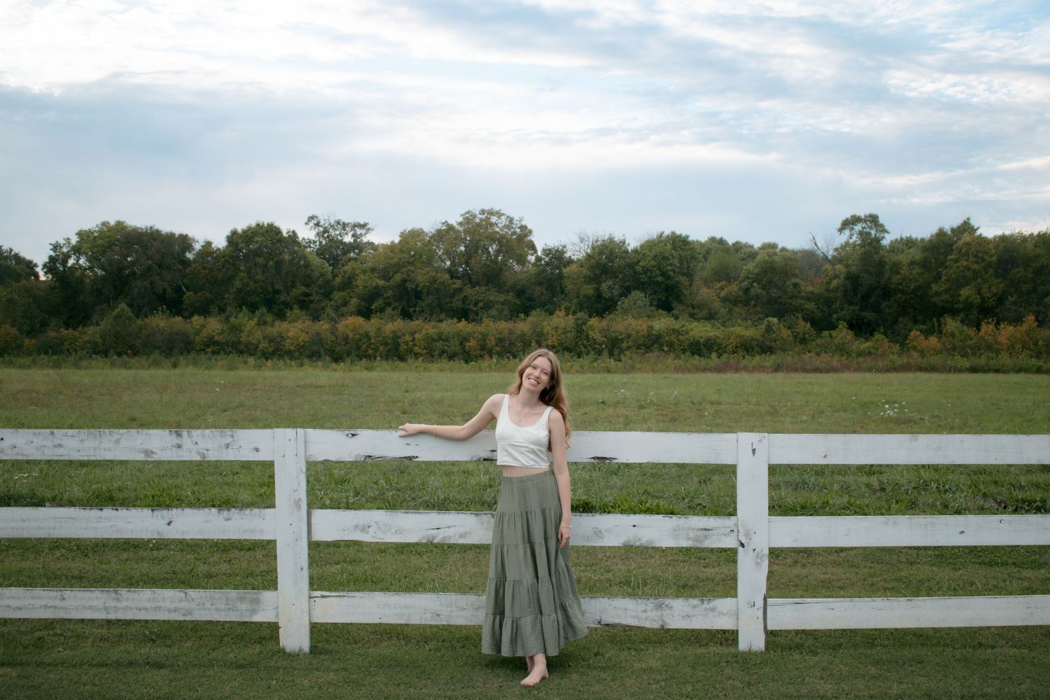 A panoramic view of a white fence stretching along a green field under a cloudy sky.